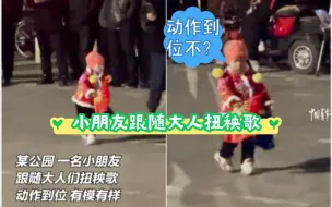 公园里，一名小朋友跟随大人们扭起秧歌，动作到位有模有样
