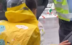 下雨天小学门口，交警熟练的为孩子开车门、穿雨衣。