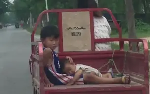 妈妈骑三轮车带俩娃回家 弟弟躺在哥哥腿上睡着了 哥哥用手默默护住弟弟的头